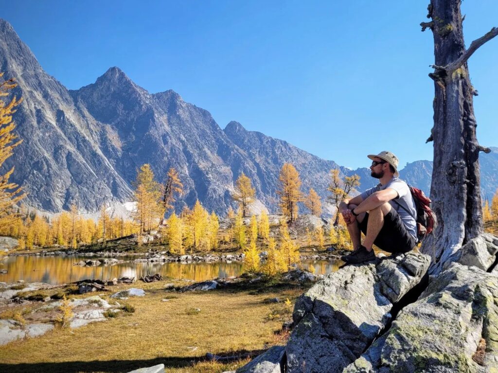 Man sitting against tree in Monica Meadows with mountains in the background