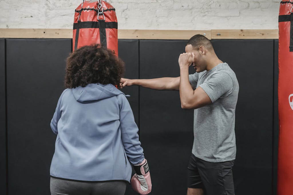 Ethnic trainer showing exercise to female in boxing club