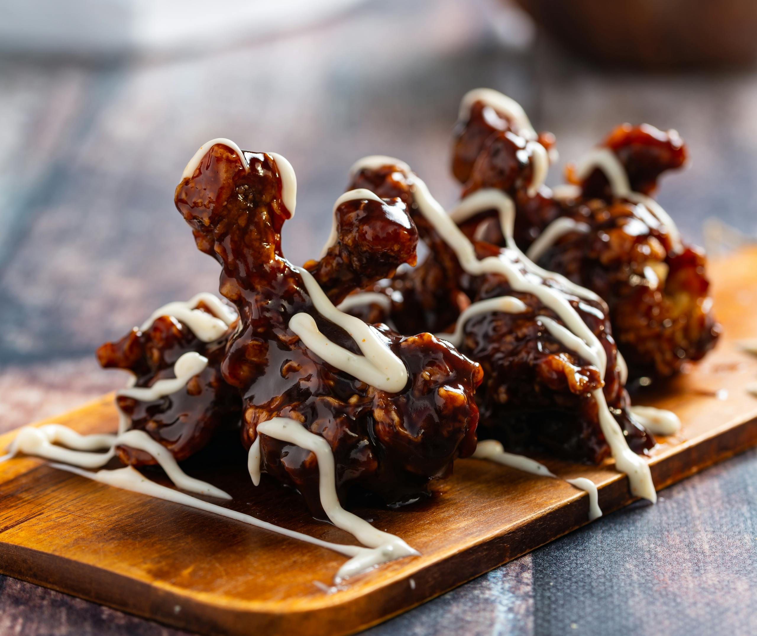 Close-up of glazed chicken wings drizzled with sauce on a wooden board.