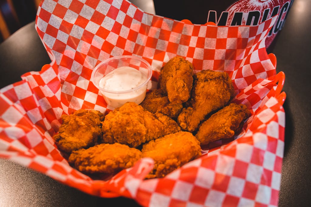 Tasty crispy fried chicken wings served with ranch dipping sauce on a checkered paper.